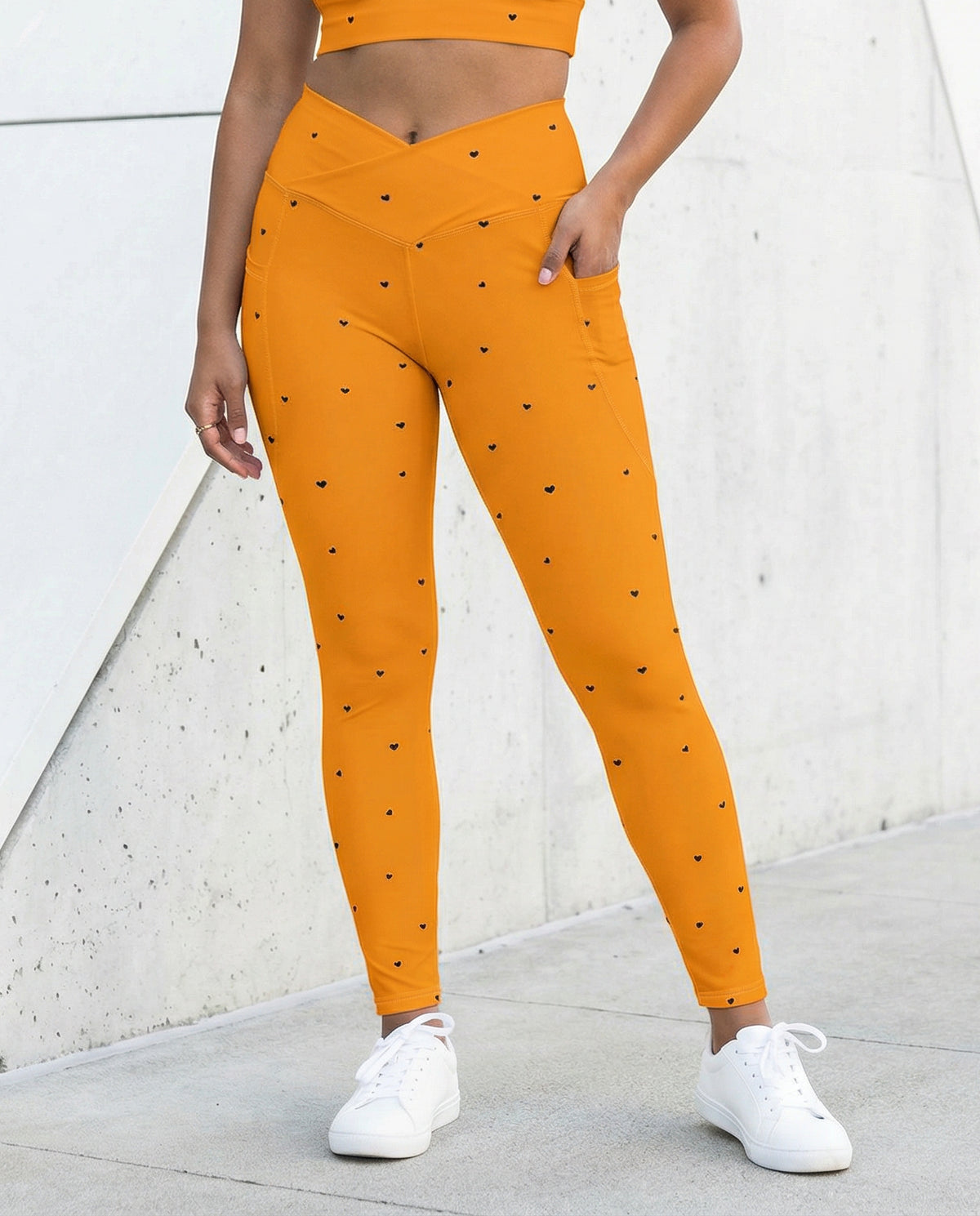 woman wearing Trixie tangerine orange crossover leggings with pockets and tiny black heart print front