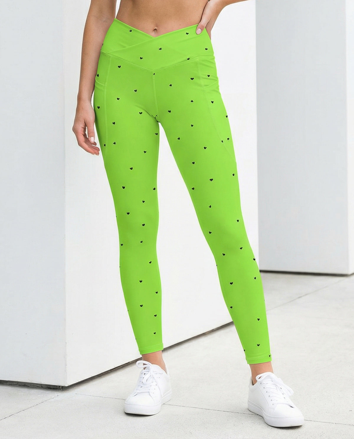 woman wearing Yasmin neon lime green crossover leggings with pockets and tiny black heart print front