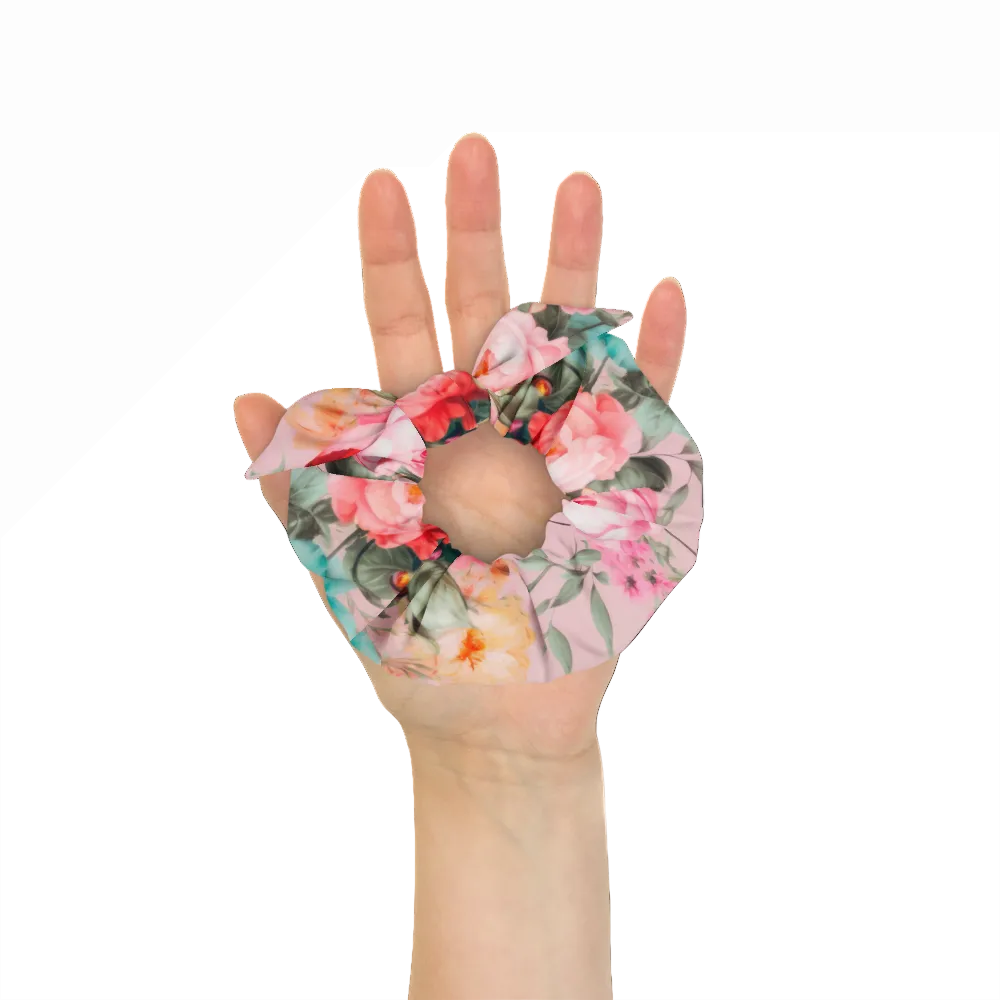 Baby pink scrunchie with feminine colorful botanical floral pattern on it with bow detail front view on a hand to show approximate scale