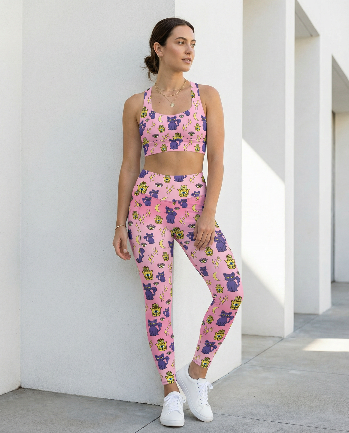 Woman wearing pink longline sports bra with purple cat and yellow evil eye pattern showing the front Full outfit of sports bra and leggings