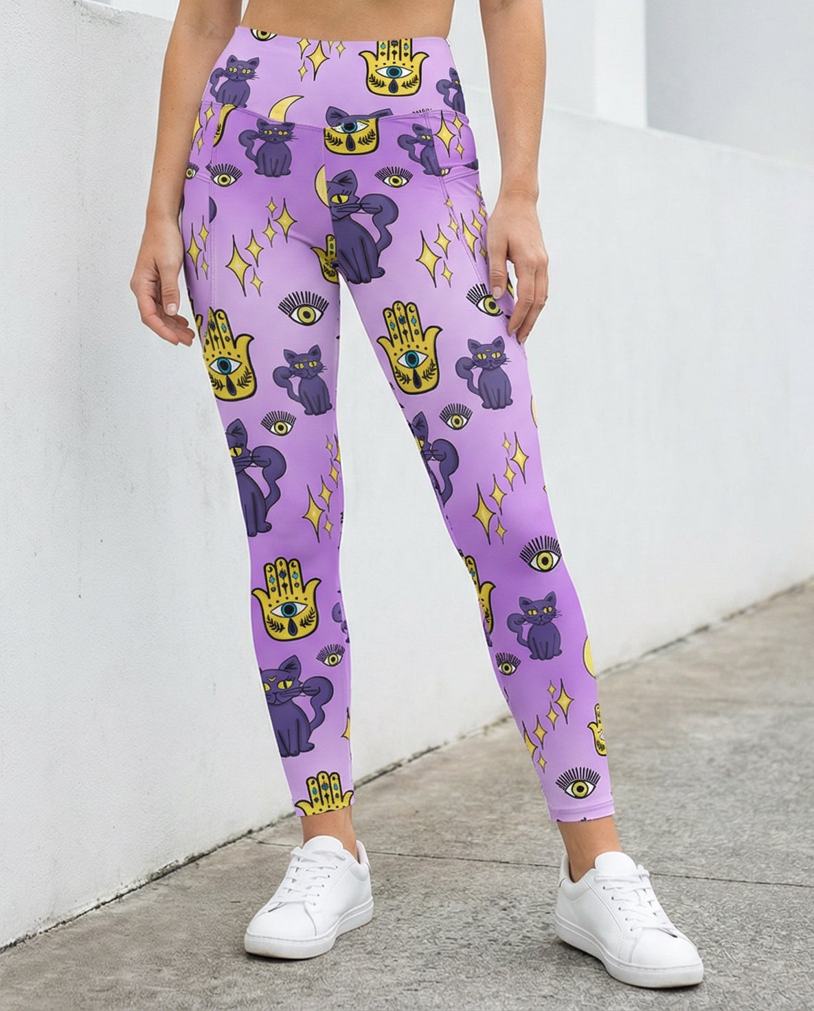 Woman wearing purple leggings with purple cats and yellow evil eye pattern on them with side pockets front view